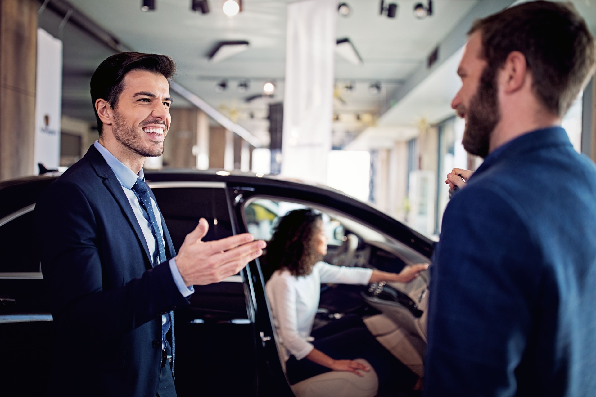 Car dealer is presenting a car to couple in a showroom